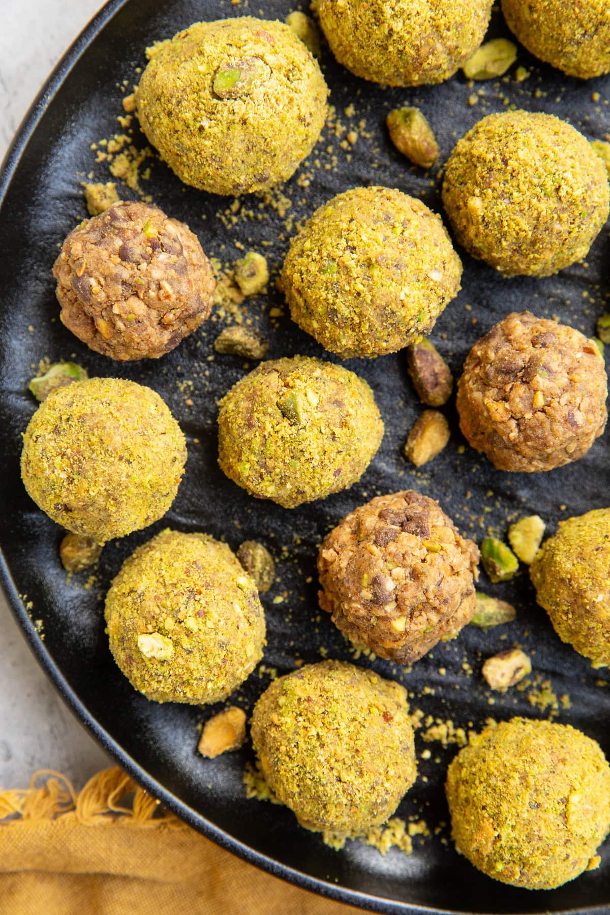 Pistachio balls on a black plate, ready to eat. Some of the balls are coated in ground up pistachios and some of them aren't.