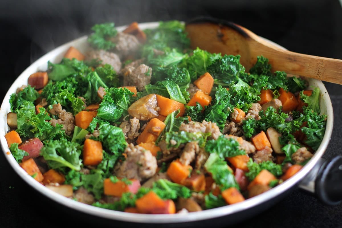 Kale, sweet potato, mushrooms, garlic, and sausage cooking in a skillet