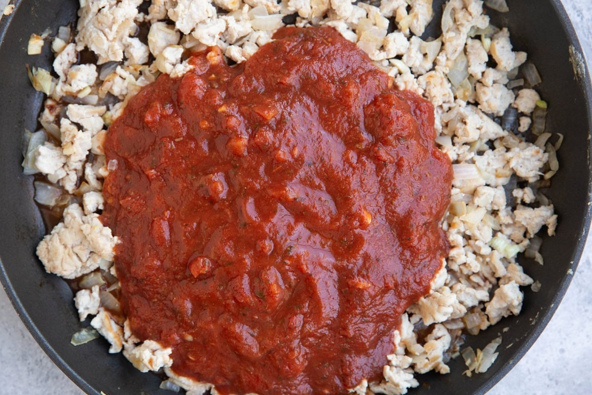 Skillet of ground turkey with tomato sauce on top, ready to be mixed in.