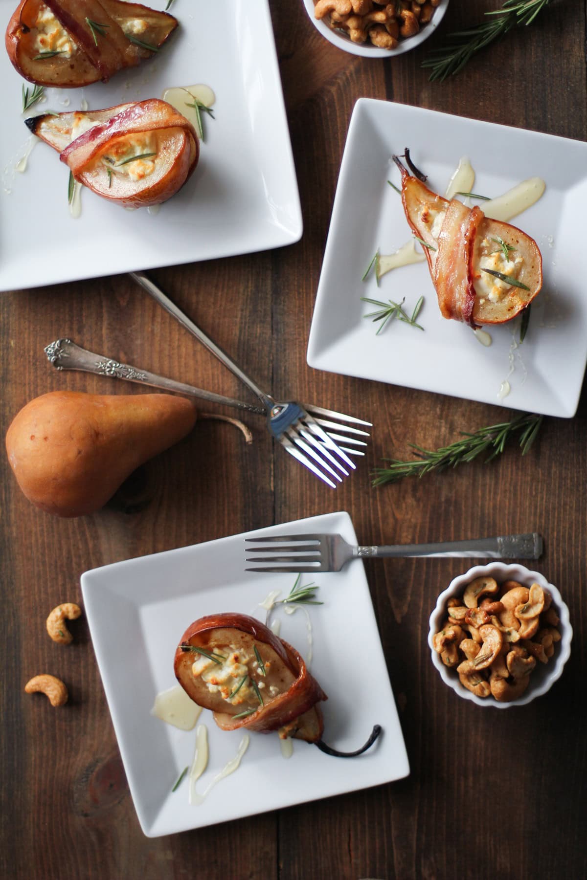 Several square white plates with bacon wrapped pears stuffed with herbed goat cheese and drizzled with honey.