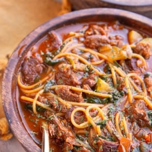 Two bowls of birria soup in wooden bowls with a golden spoon, ready to serve.
