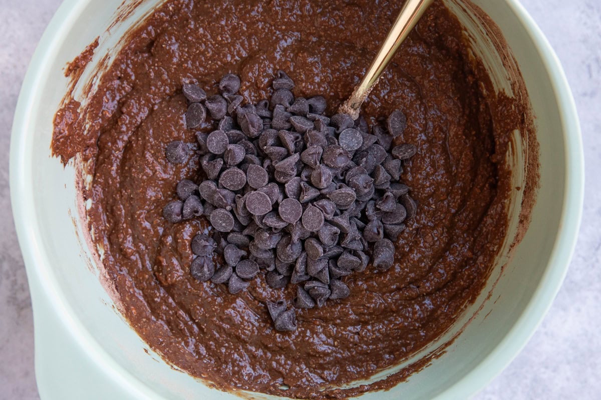 Mixing bowl with chocolate bread batter inside with chocolate chips sitting on top, ready to be mixed in.