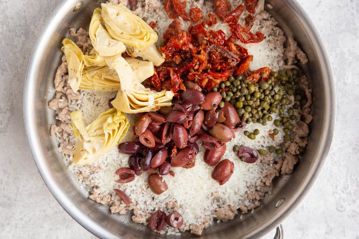 Ground turkey, rice, sun-dried tomatoes, capers, artichoke hearts in a stainless steel skillet.