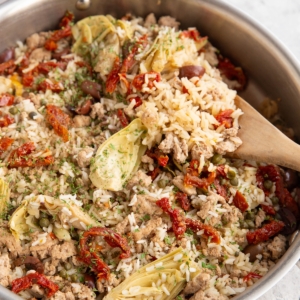 Stainless steel skillet full of ground turkey, rice, and veggies with a wooden spoon scooping some of it out.