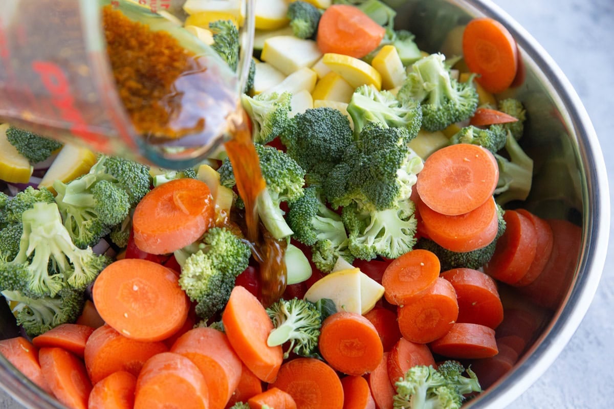 Large bowl of chopped vegetables with sauce being poured