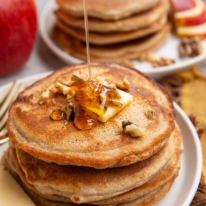 Stack of apple pancakes with butter and chopped pecans on top being drizzled with honey.