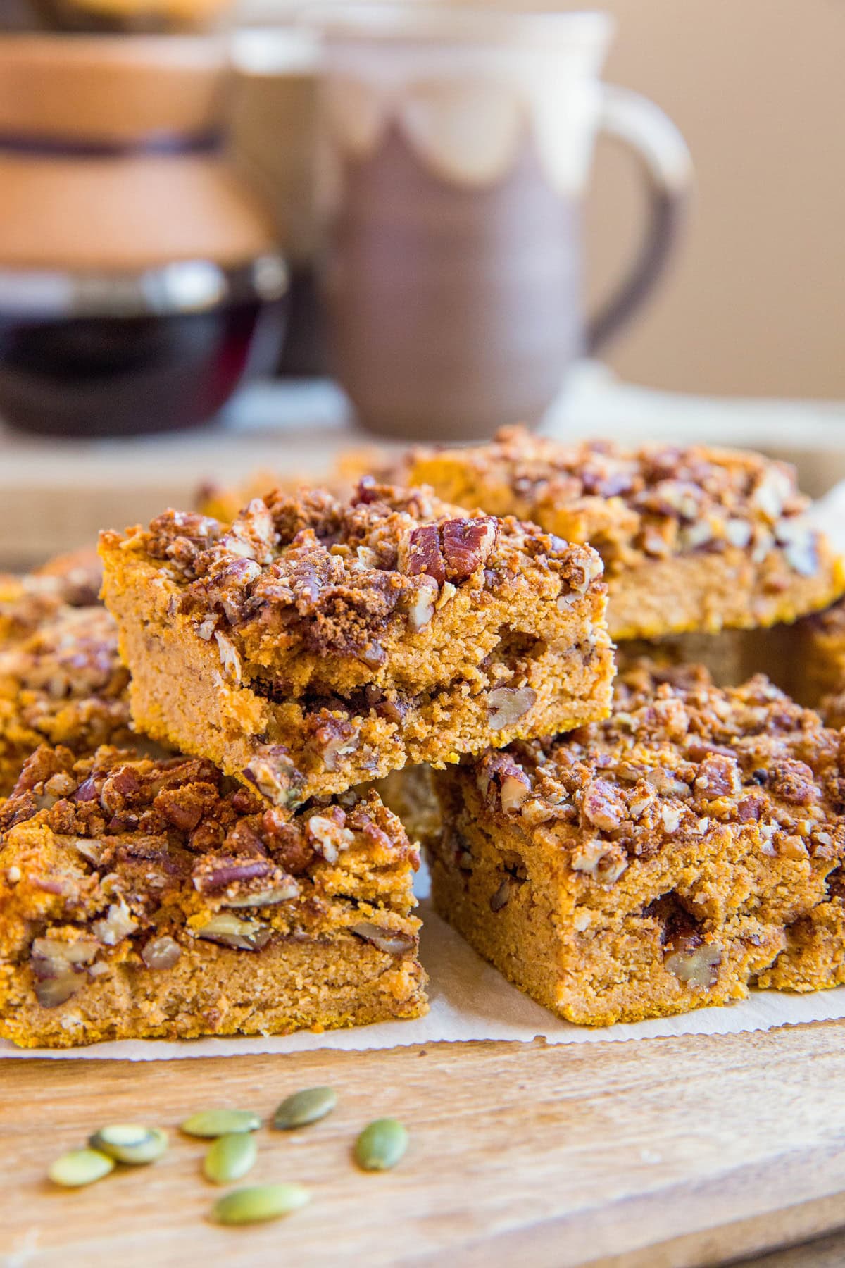 Slices of pumpkin coffee cake on a wooden cutting board with a mug and a chemex of coffee in the background.