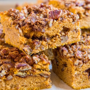 Slices of Pumpkin Coffee Cake stacked on a wooden cutting board with pumpkin seeds sprinkled around.