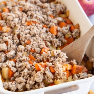 Casserole dish of sweet potato apple casserole with a wooden spoon inside the casserole, ready to serve.