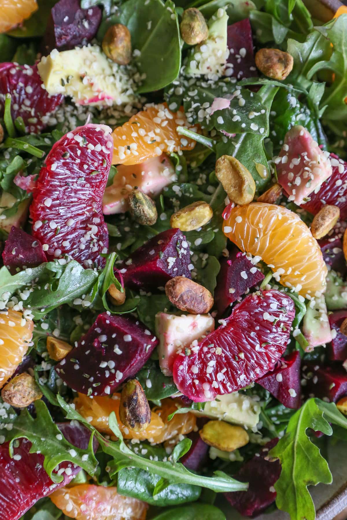 Close up on salad with peeled mandarins and blood oranges, arugula, spinach, hemp seeds, pistachios, roasted beets, and pistachios with citrus dressing.