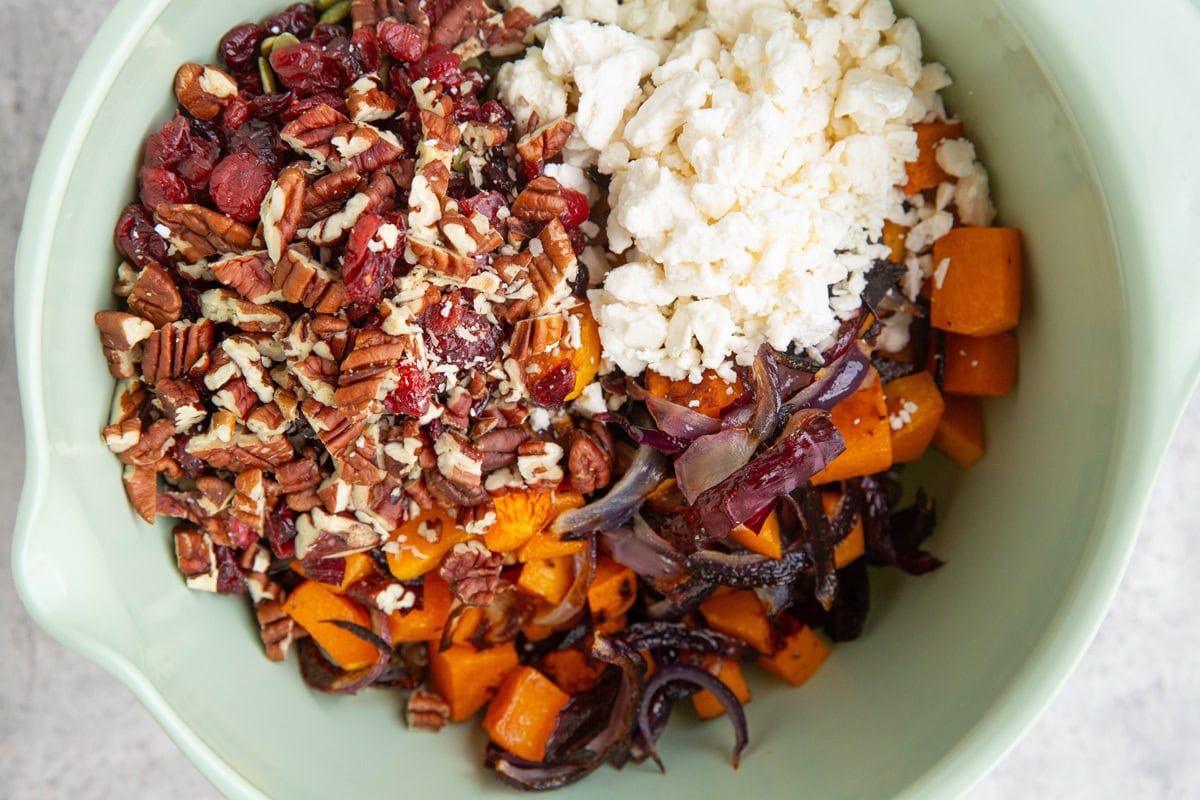 Mixing bowl full of roasted butternut squash, onions, dried cranberries, pecans, and feta cheese to make lentil salad.