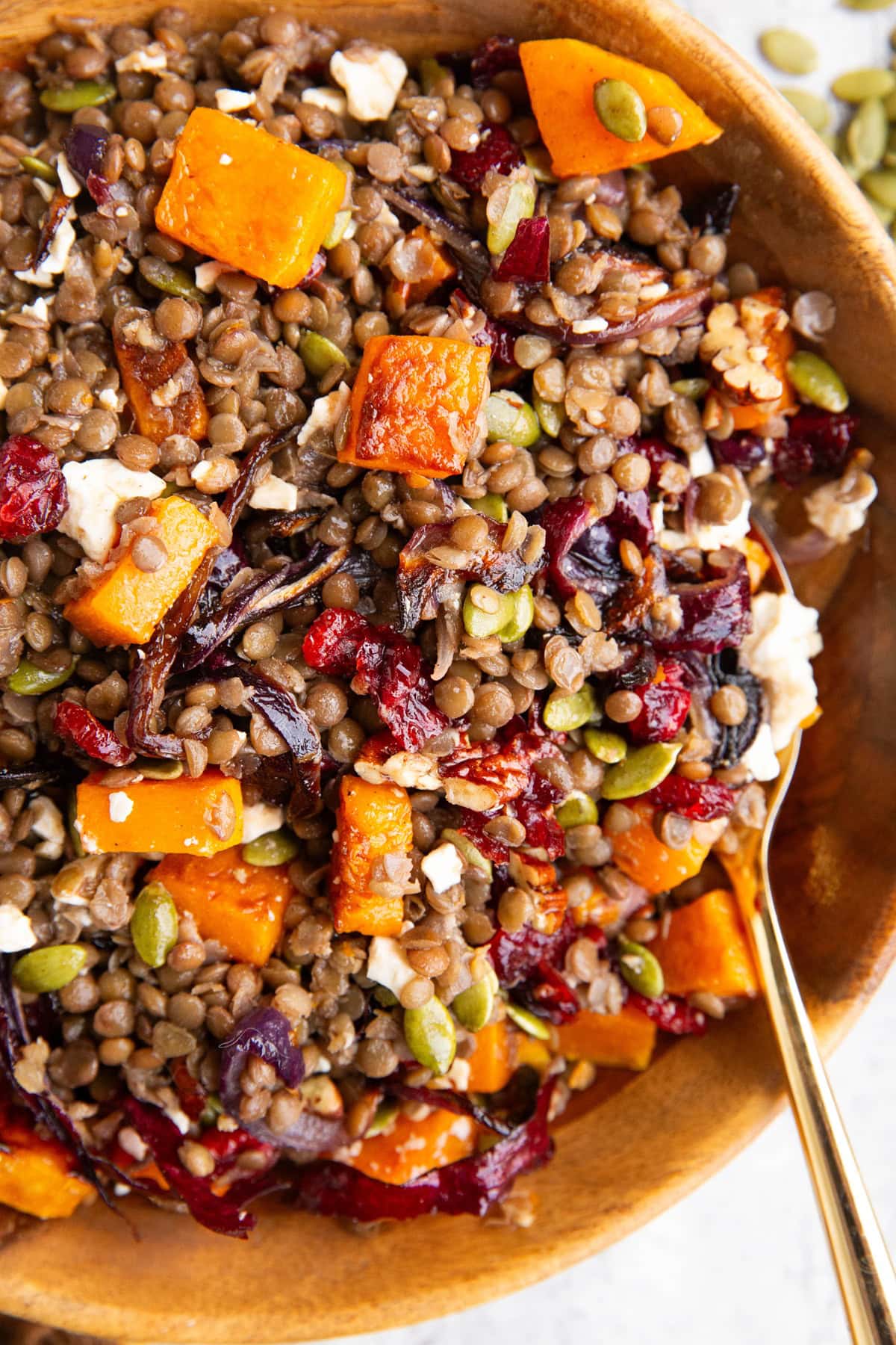 Butternut squash and lentil salad in a large wooden bowl with a golden spoon, ready to serve.