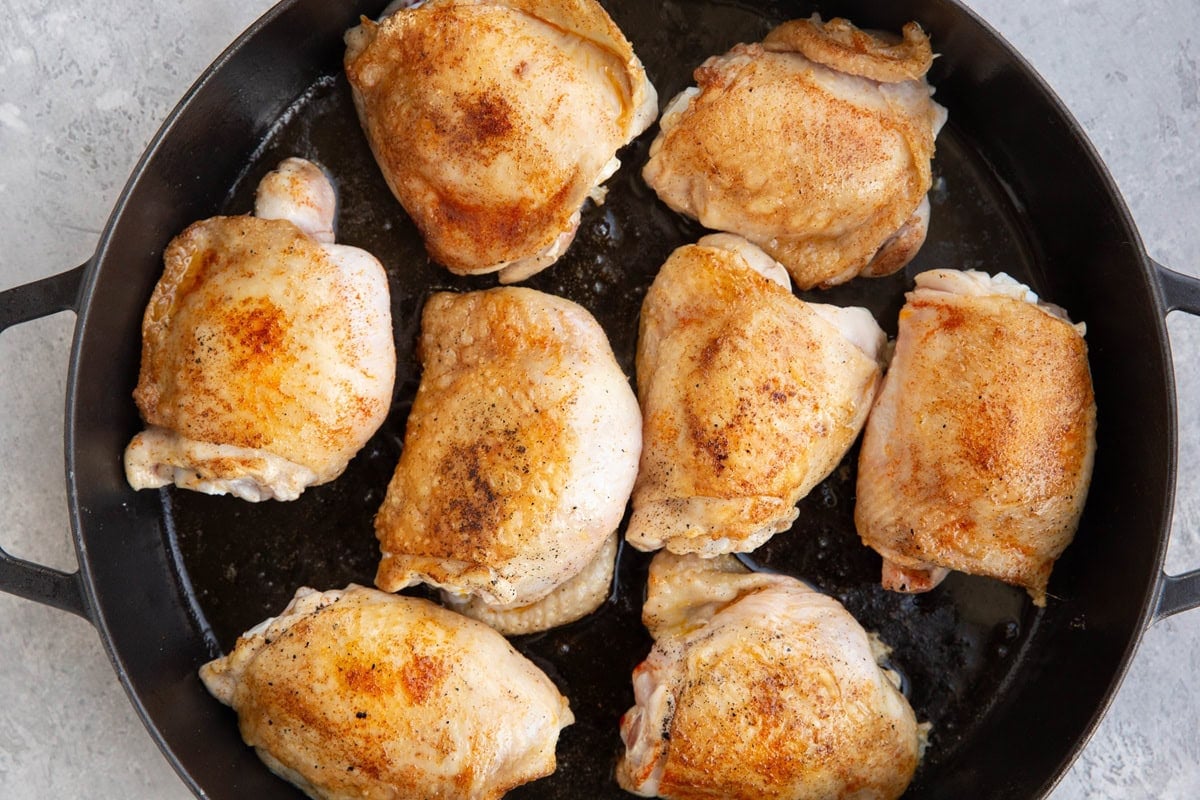 Large cast iron skillet with golden brown chicken thighs, pre-cooking before slow cooking.