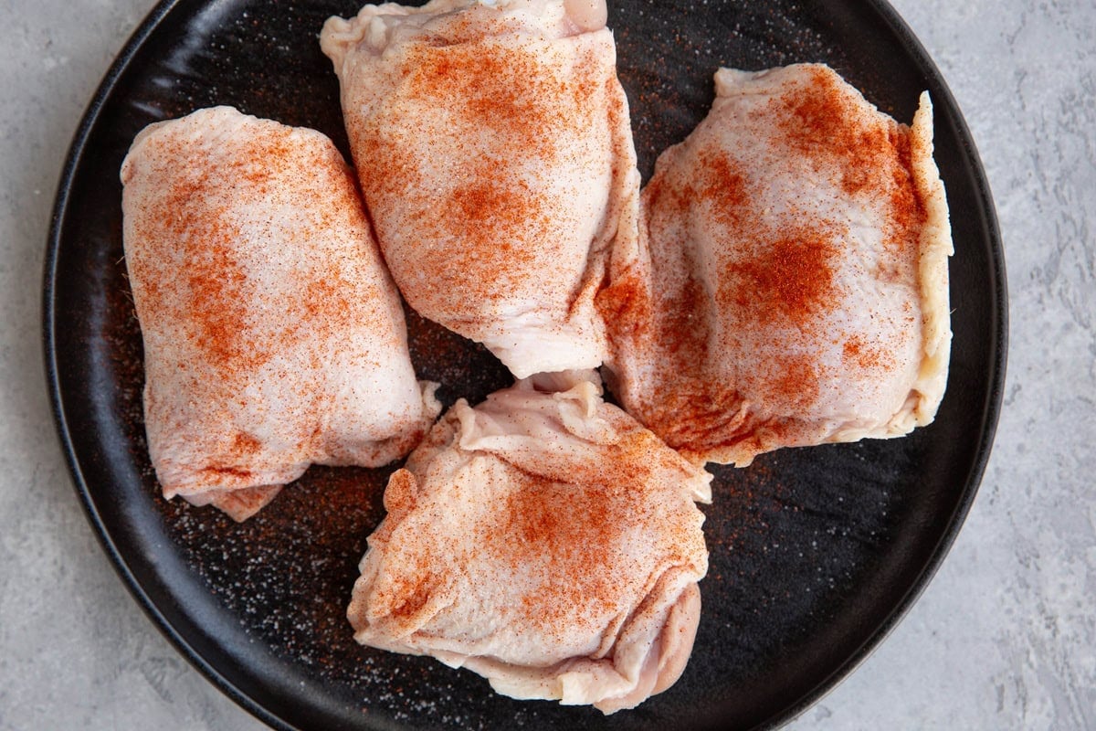Plate with four bone-in skin on chicken thighs sprinkled with paprika and sea salt.