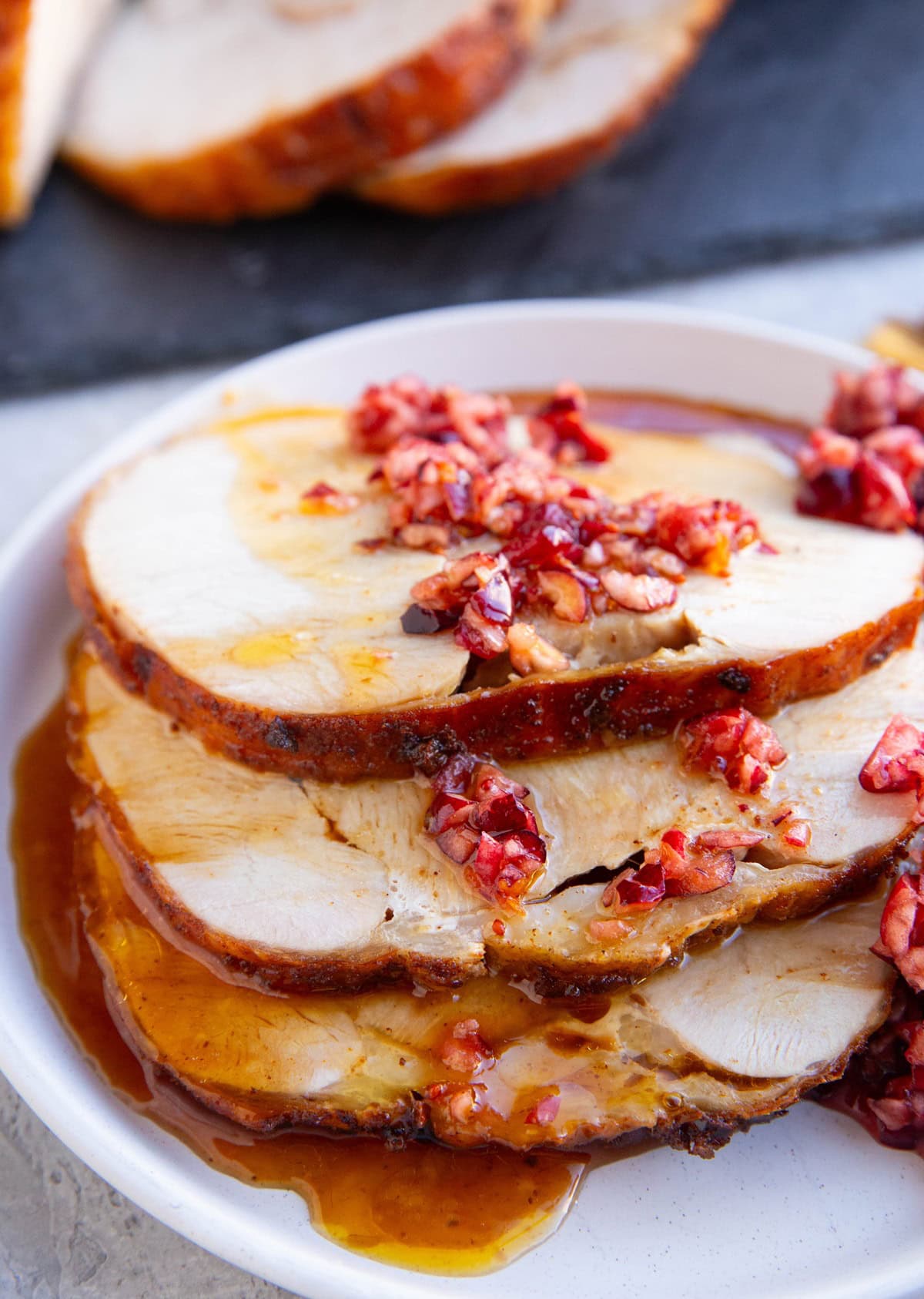 Sliced turkey roast on a white plate drizzled with cranberry relish and drizzled with turkey juices, ready to eat.
