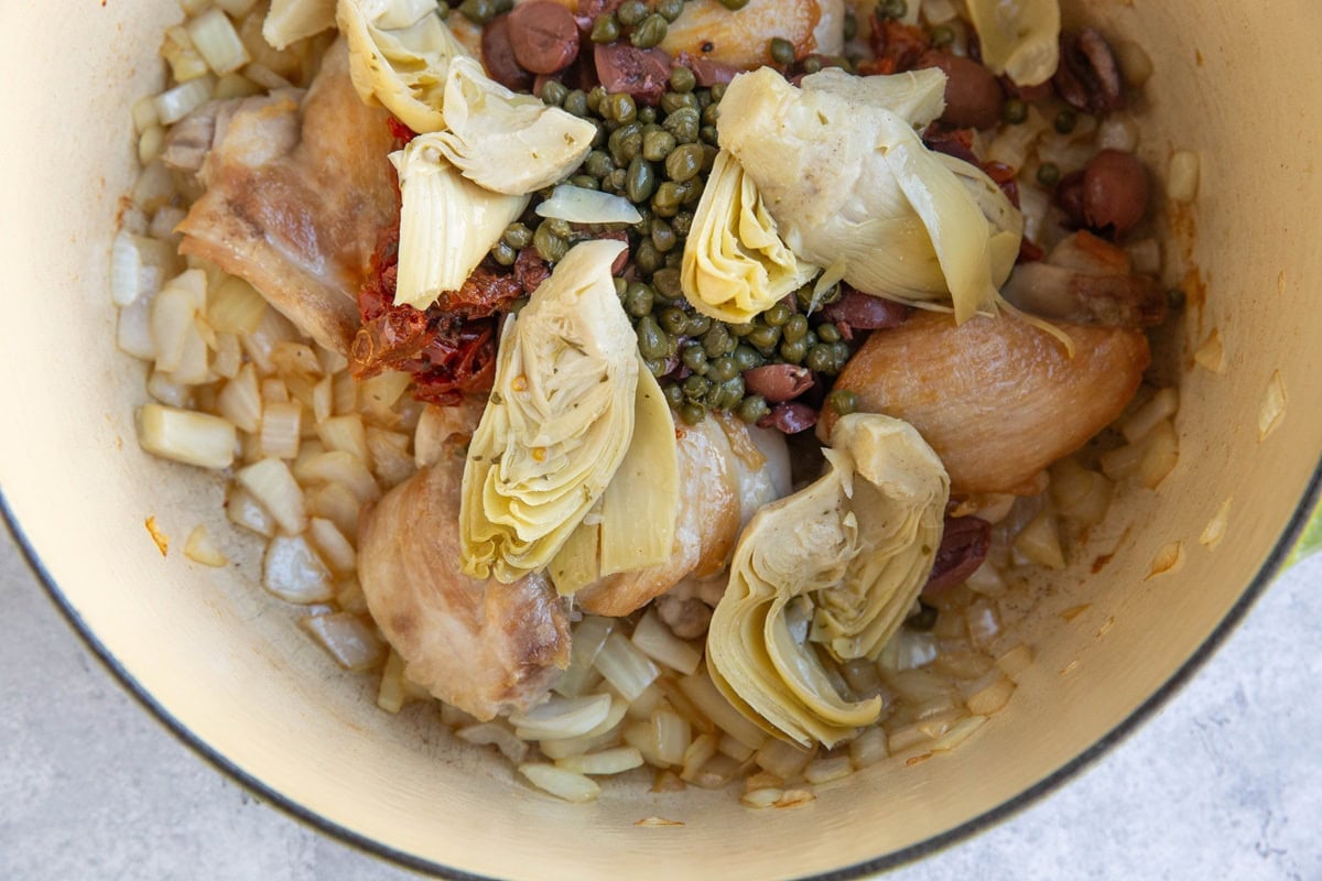 Large pot full of sauteed onion, chicken, artichoke hearts, sun-dried tomatoes, kalamata olives, and capers to make soup.