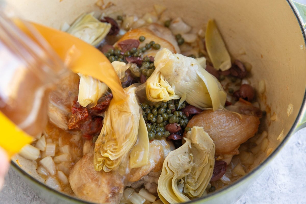 Pouring broth into a pot with the rest of the soup ingredients.