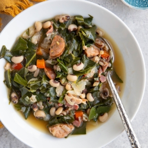 Large white bowl of black eyed pea soup with collard greens and sausage.
