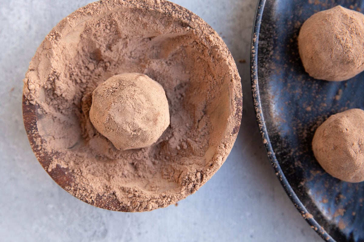 Chickpea chocolate truffle rolled in cocoa powder in a bowl to demonstrate how to coat the outside of truffles.