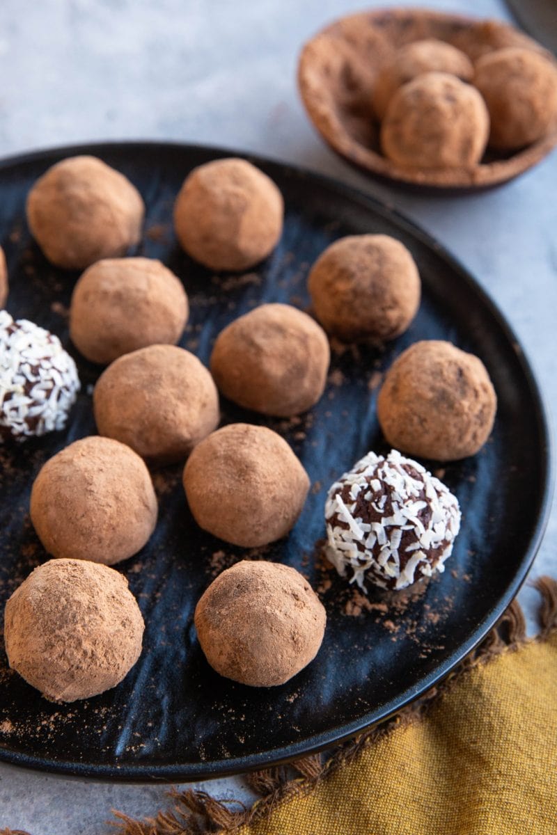 Black plate full of chocolate truffles that are coated with cocoa powder and two are covered with shredded coconut. Ready to serve.