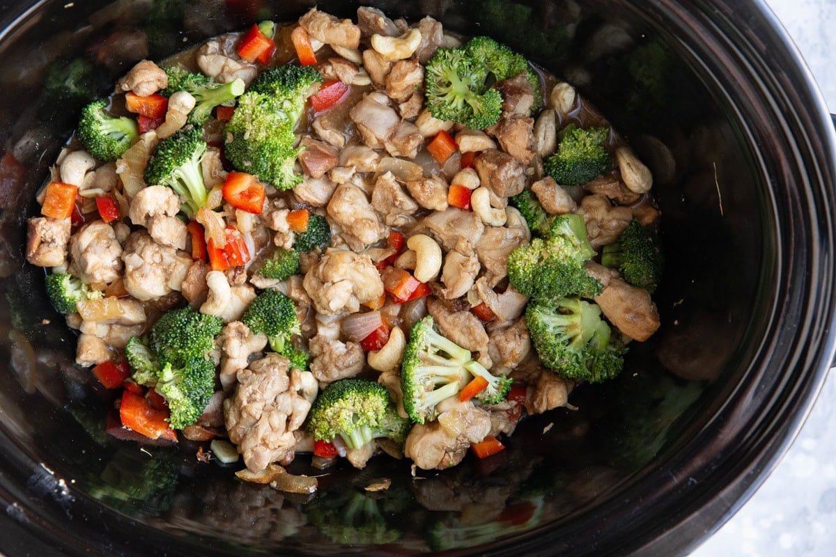 Crock pot full of cashew chicken with bell pepper and broccoli florets.