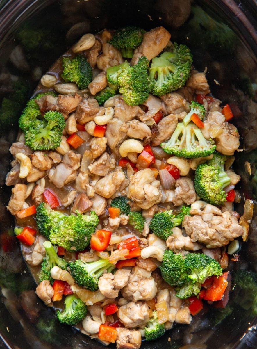 Slow cooker full of cashew chicken with fresh broccoli and bell peppers, ready to eat.