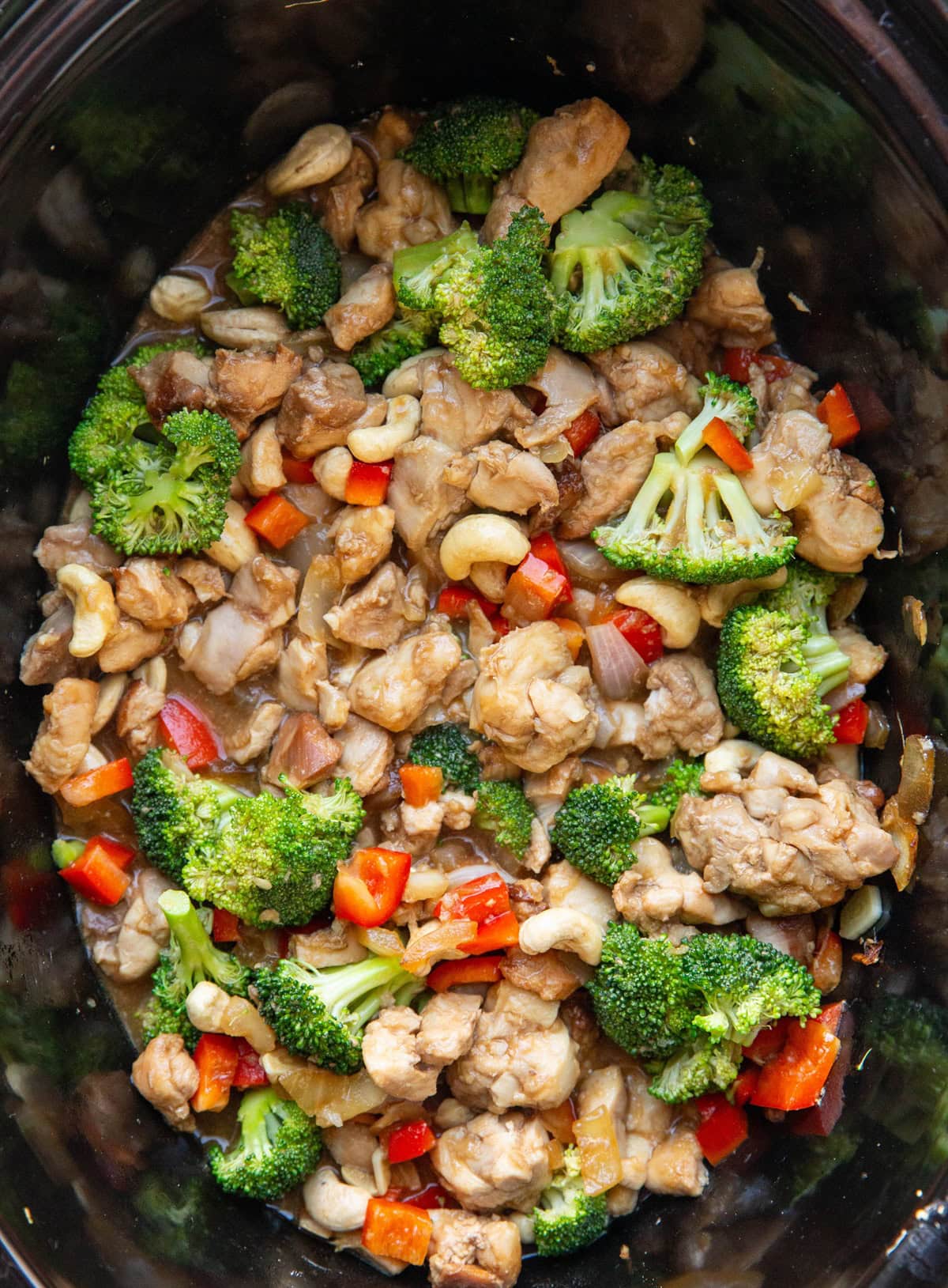 Slow cooker full of cashew chicken with fresh broccoli and bell peppers, ready to eat.