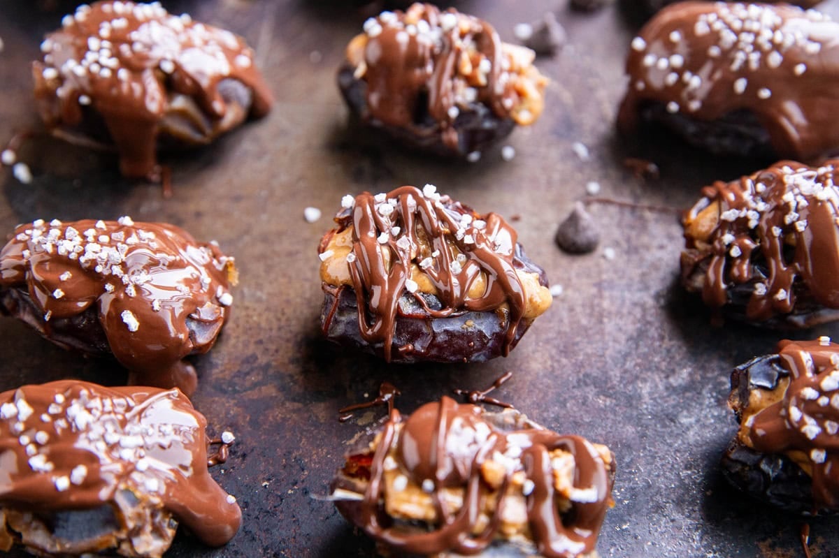 Dates stuffed with peanut butter on a baking sheet drizzled with melted chocolate and sprinkled with sea salt.