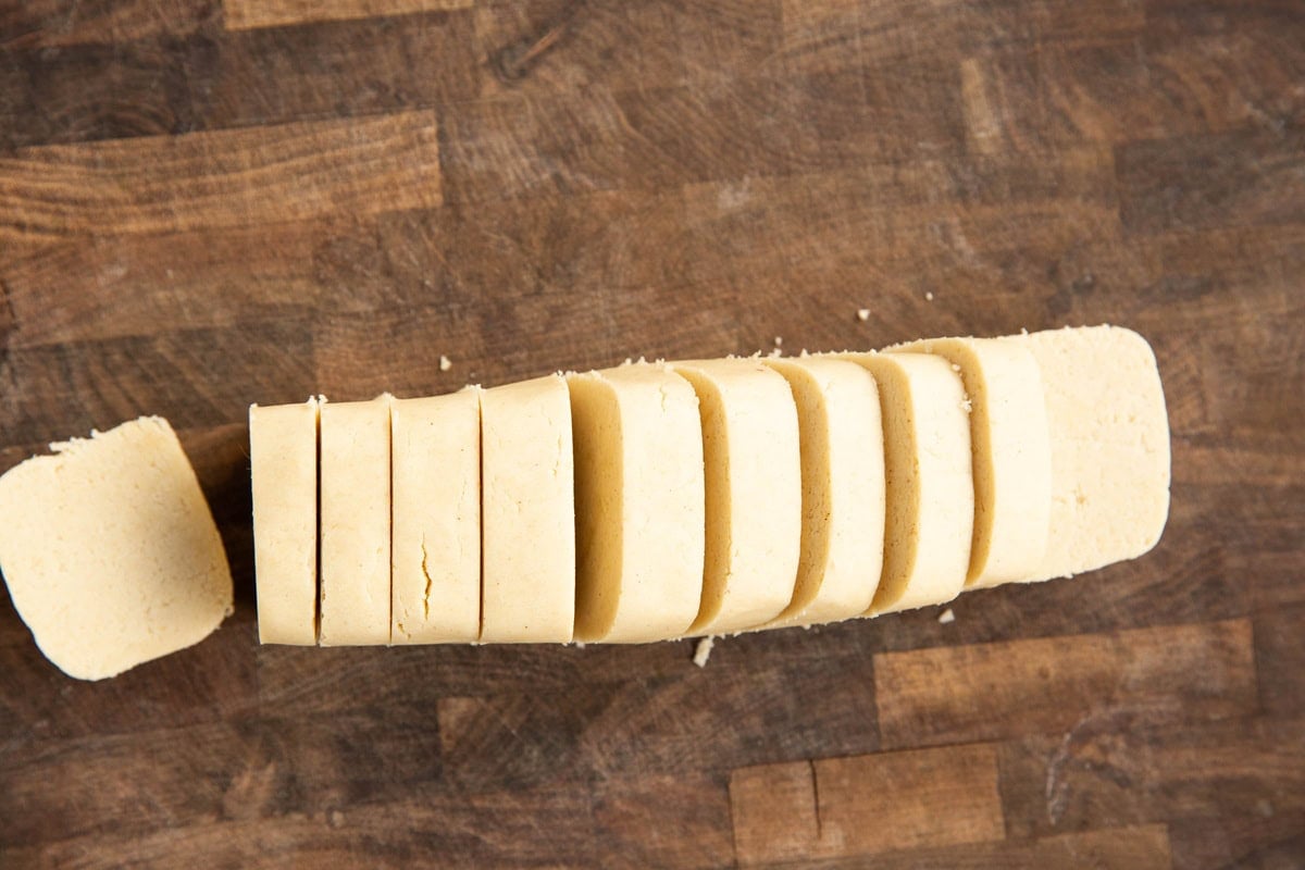 Cutting board with shortbread cookie dough cut into slices.