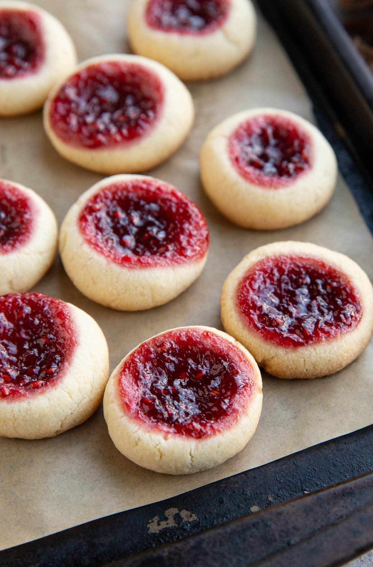 Many raspberry thumbprint cookies on a baking sheet, fresh out of the oven and ready to serve.