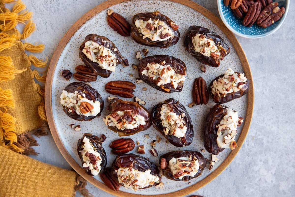 Plate full of ricotta stuffed dated with a small bowl of pecans to the side and a golden napkin, ready to serve.