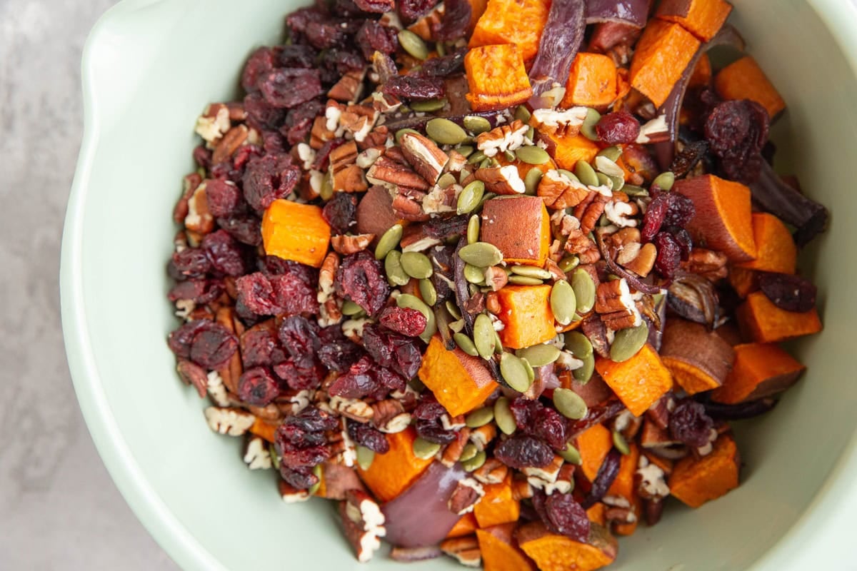 Mixing bowl full of cooked brown rice, roasted sweet potatoes, onions, pecans, dried cranberries, and pumpkin seeds.