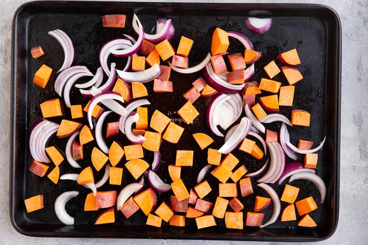 Chopped sweet potatoes and onions on a large baking sheet, ready to be roasted.