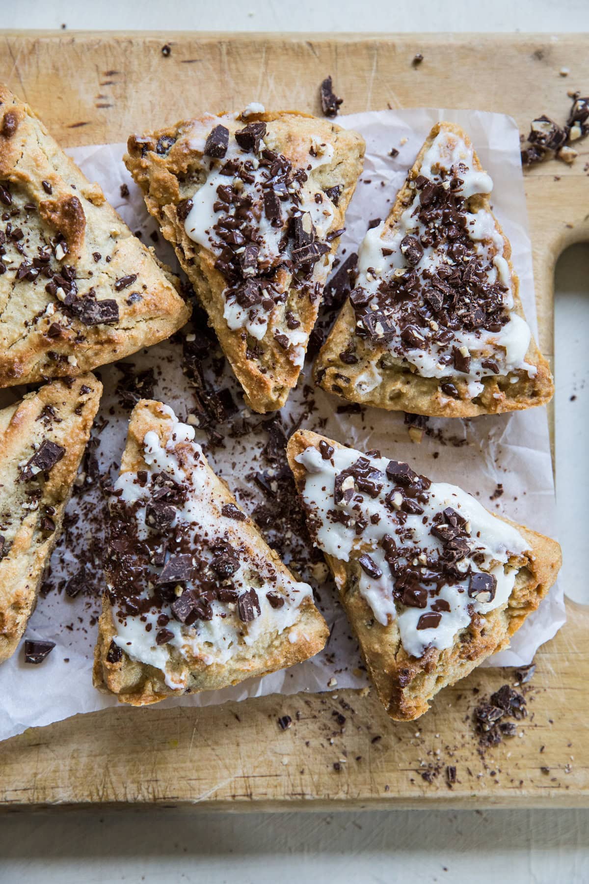 Wooden cutting board with six chocolate chip scones on top covered with glaze and more chopped dark chocolate. Ready to serve.