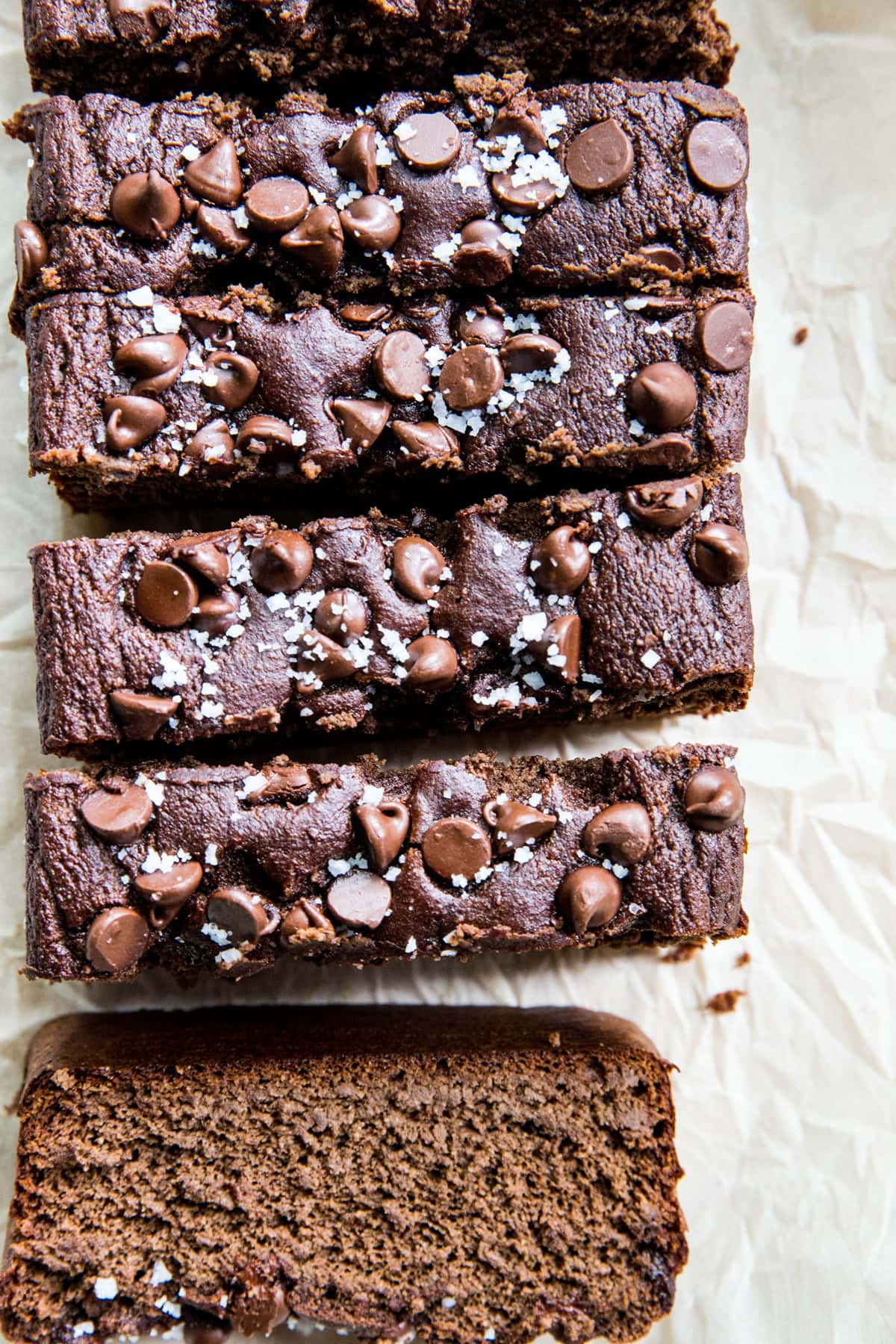 Loaf of chocolate banana bread cut into individual slices. Chocolate chips and sea salt are sprinkled on top.