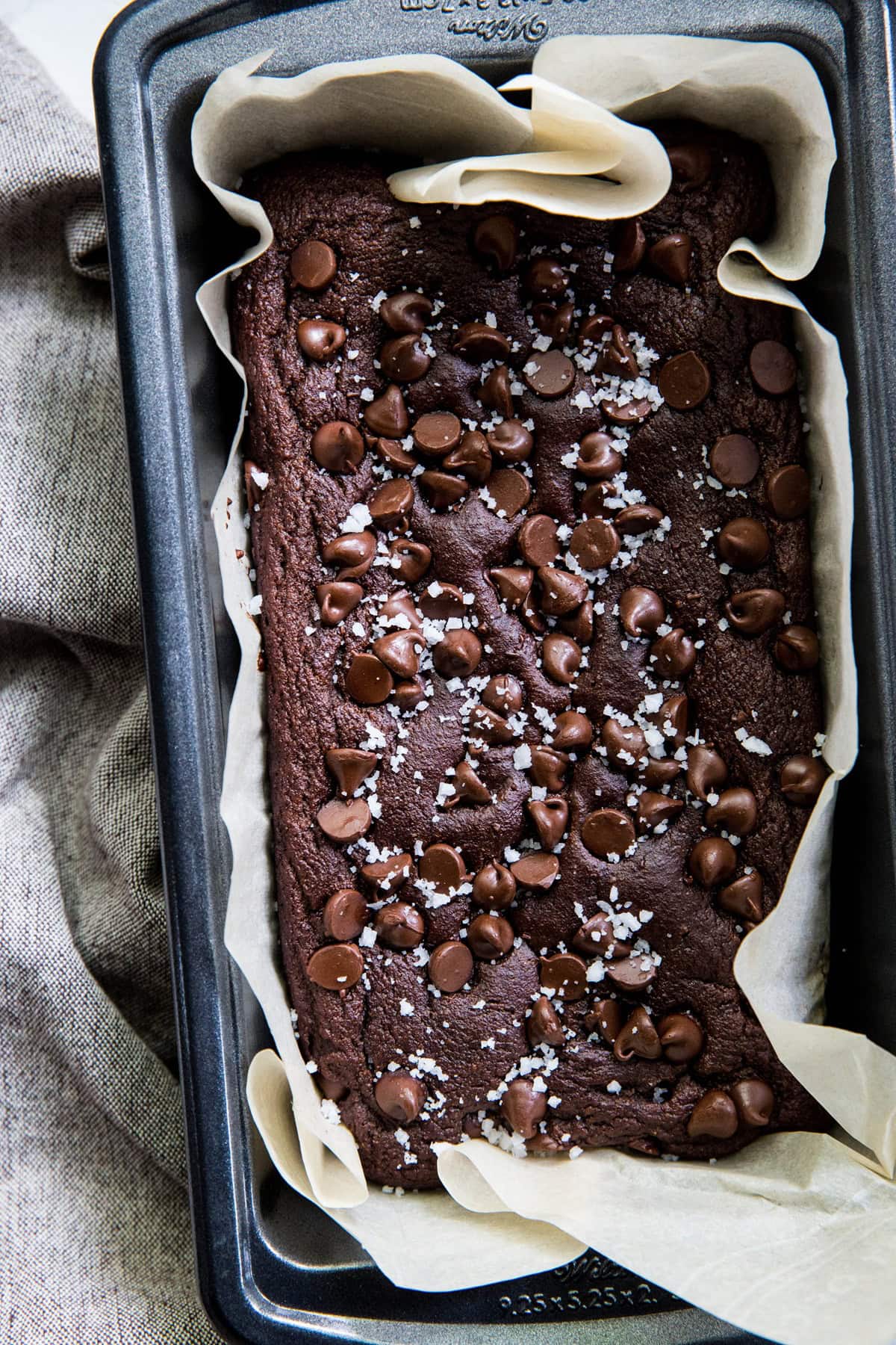 Bread pan with chocolate banana bread inside with chocolate chips and flakey sea salt on top.