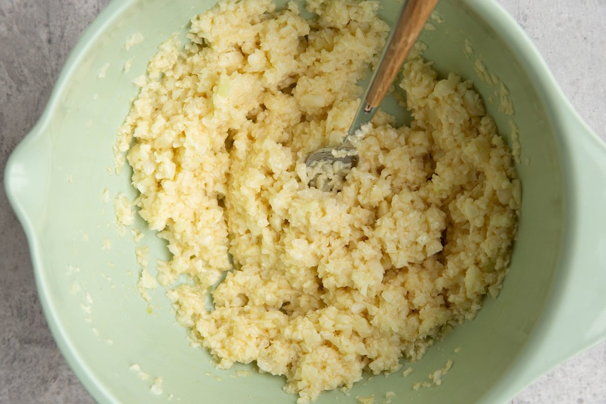 Mixing bowl full of cauliflower pieces mixed with beaten egg to make hash browns.