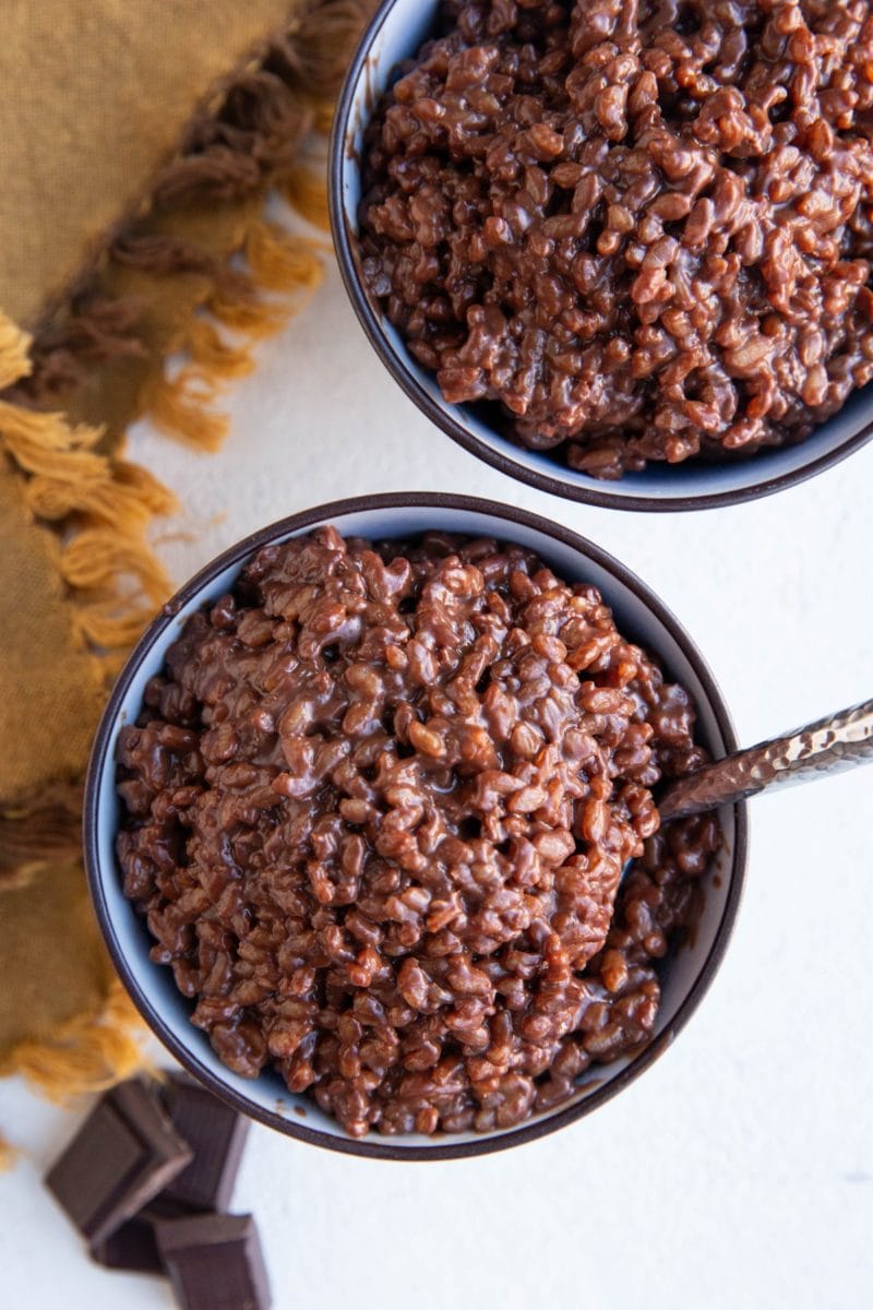 Two bowls of chocolate rice pudding with dark chocolate to the side.