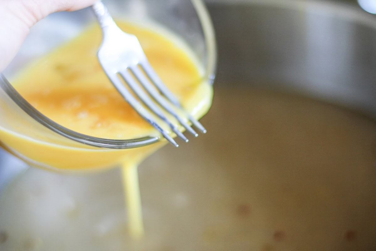 Pouring beaten eggs through the tines of a fork into a pot of broth to make egg drop soup.