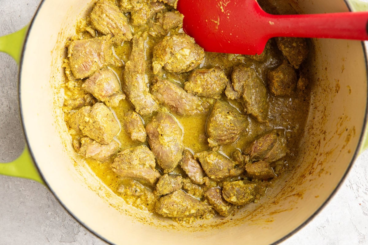 Large Dutch oven full of lamb meat cooked in a marinade.