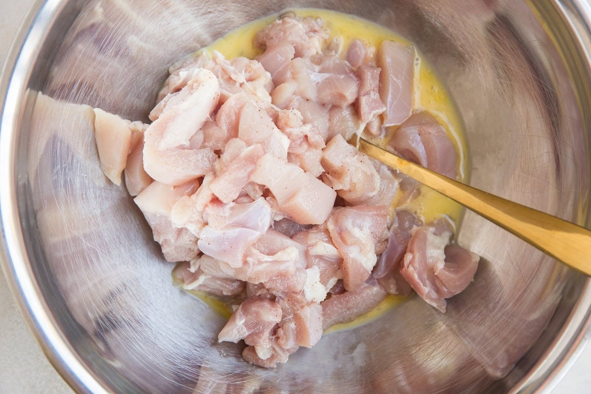 Stainless steel bowl full of chopped chicken with beaten egg to mix together to coat the chicken.