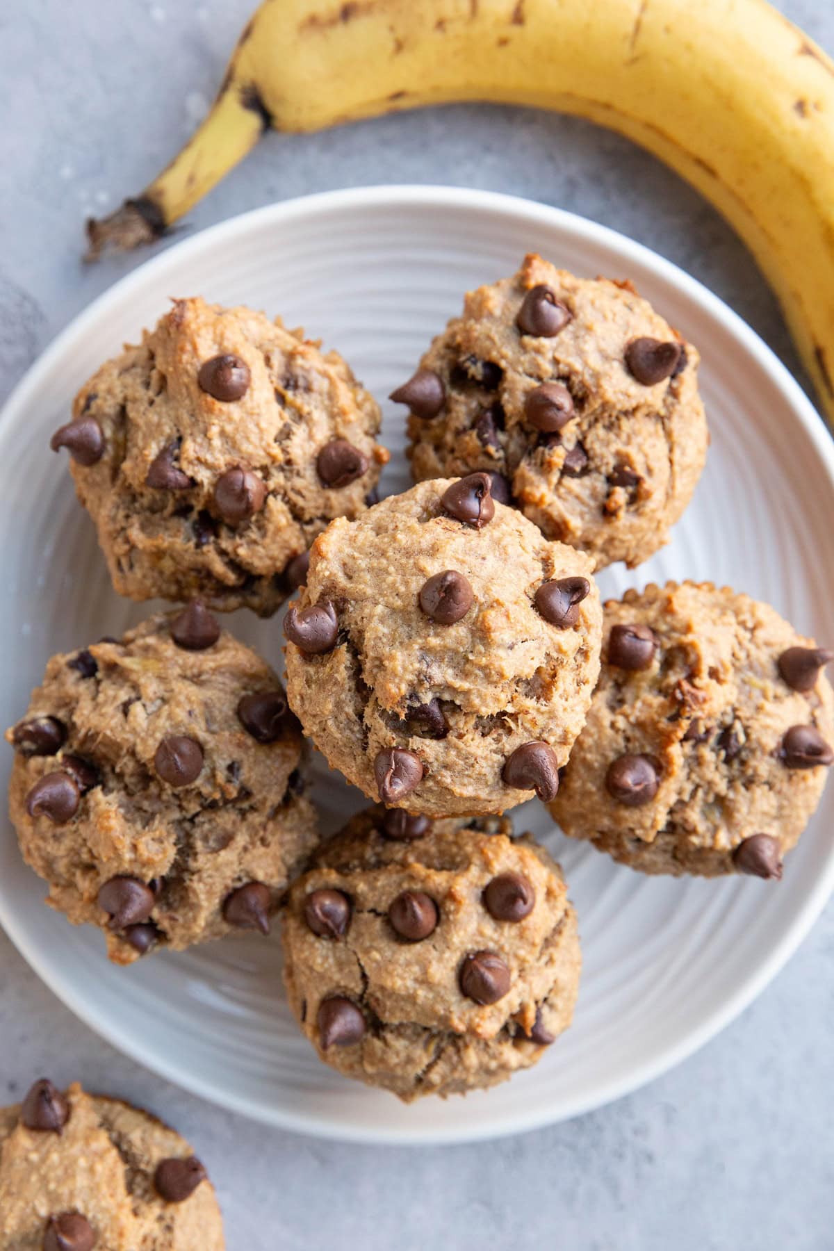 White plate with six peanut butter banana muffins and a ripe banana to the side.