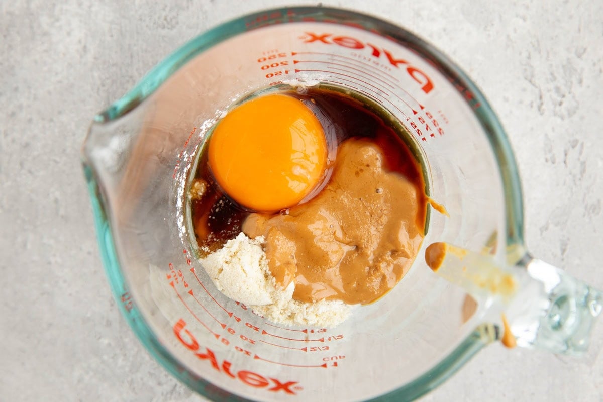 Measuring cup full of ingredients for an almond flour peanut butter mug cake.