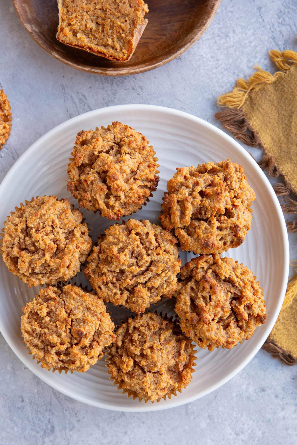 White plate of sweet potato muffins with a golden napkin to the side and a wooden plate with a muffin sliced in half.