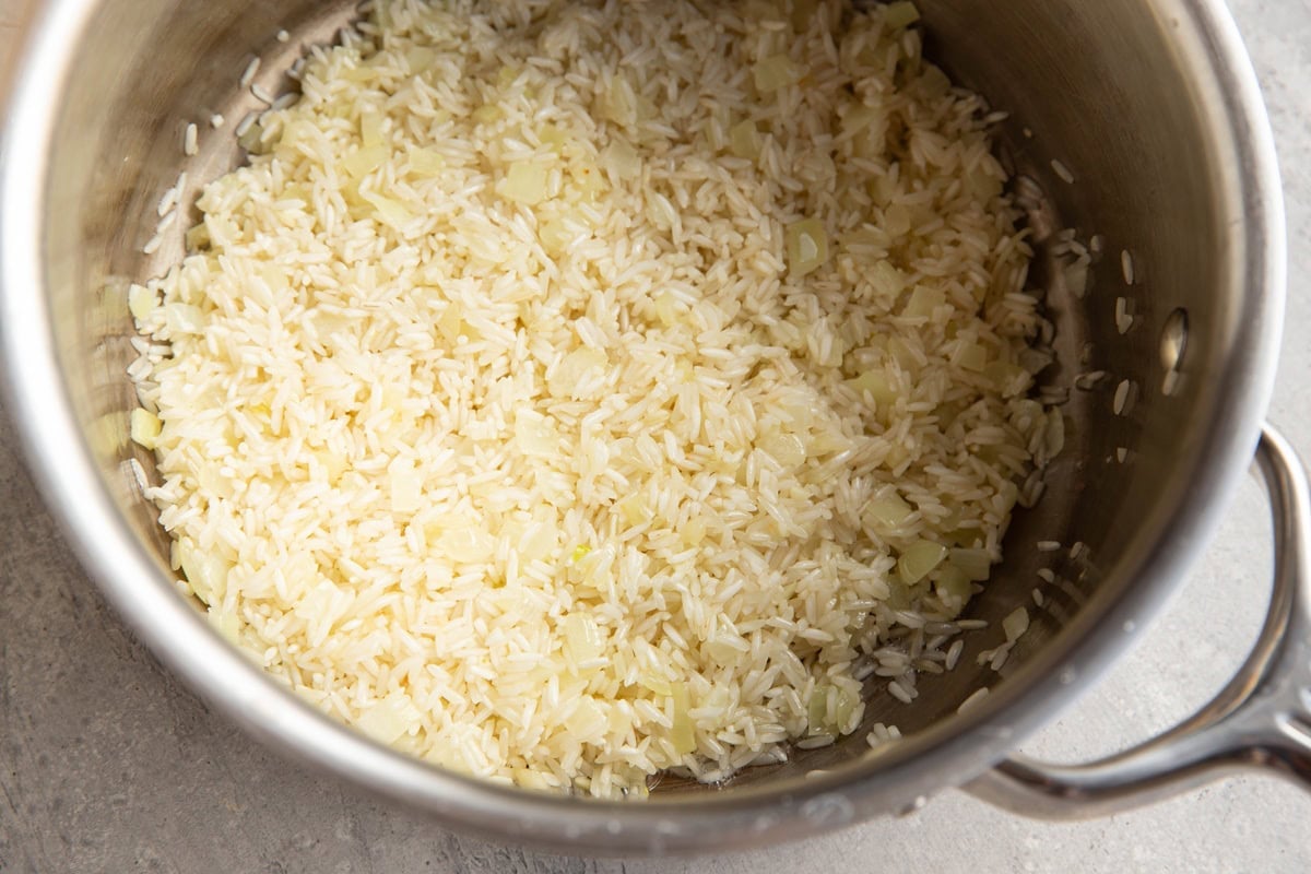 Saucepan with white rice, onion, and garlic sautéing to make a rice dish.