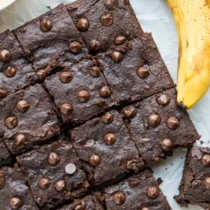 Square shaped chocolate cake cut into individual portions with ripe bananas next to the cake.