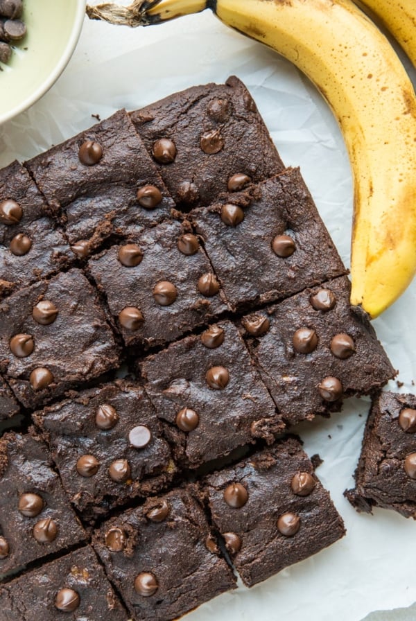 Square shaped chocolate cake cut into individual portions with ripe bananas next to the cake.