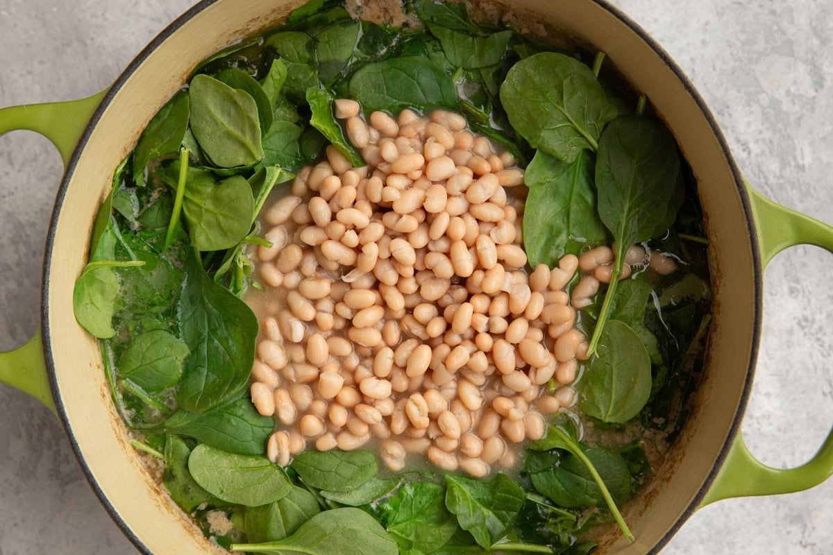 Large pot of soup with spinach and white beans on top.