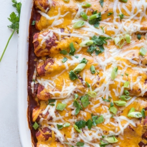 Casserole dish full of pork enchiladas with shredded cheese, chopped green onions, and parsley on top. Fresh out of the oven and ready to serve.