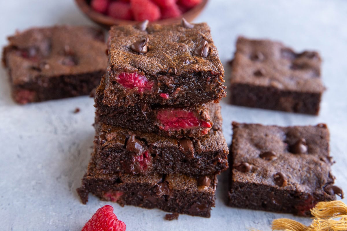 Stack of four raspberry brownies with more brownies around.